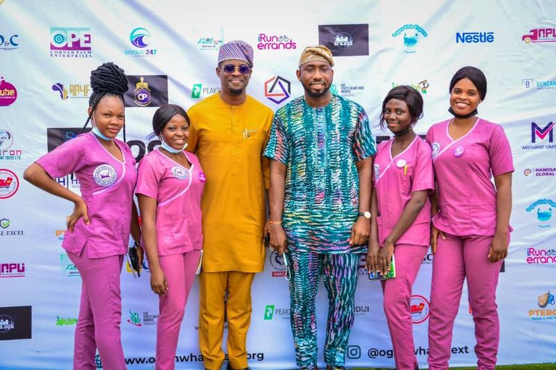 A group of attendees, several in matching uniforms, in front of the branded media wall.